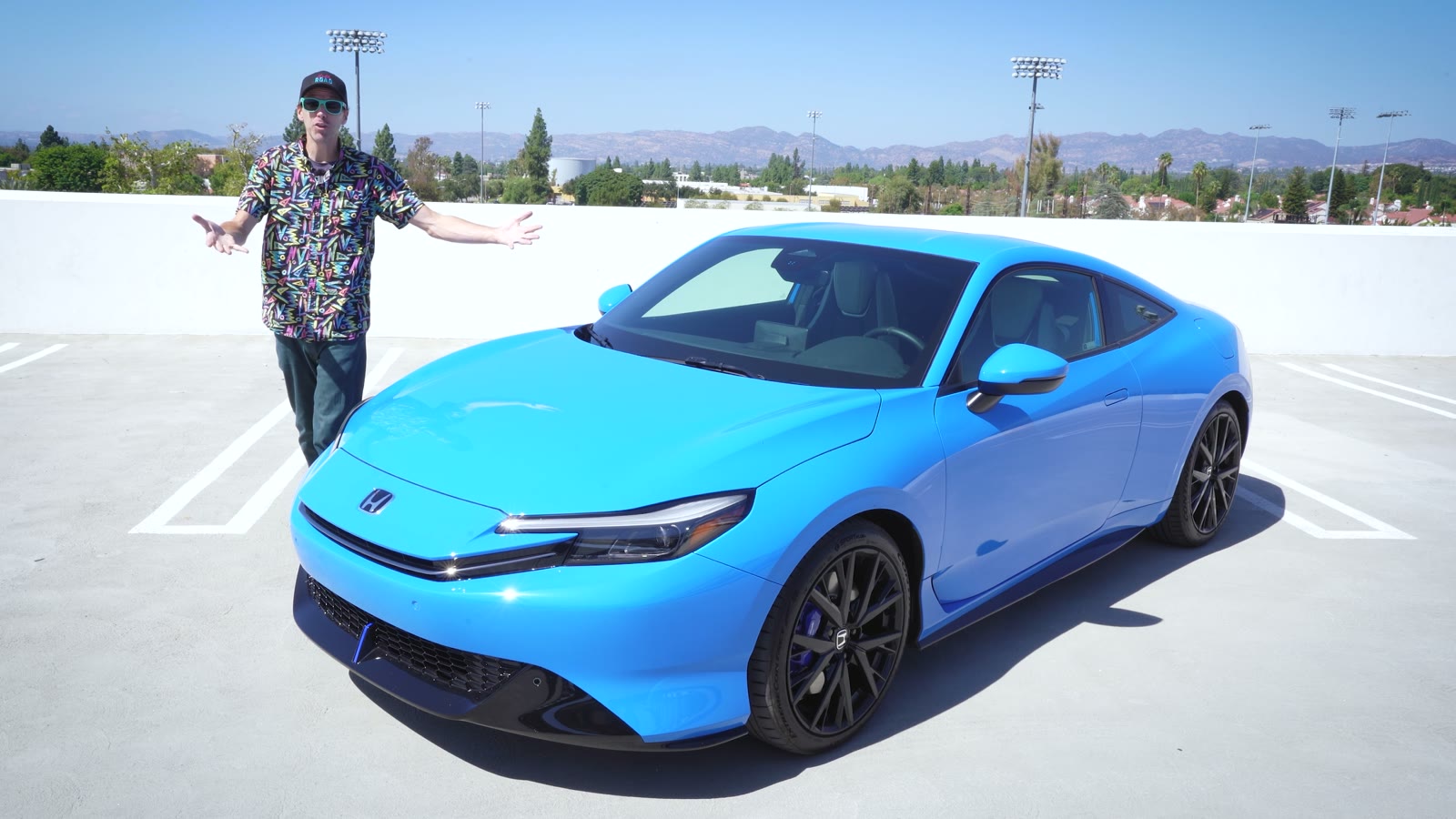Ethan Tufts standing beside a blue 2026 Honda Prelude on a rooftop parking deck